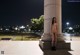 A naked woman standing in front of a column at night.