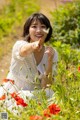 A woman in a field of red flowers pointing at the camera.