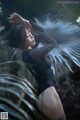 A woman in a black bodysuit posing in front of a palm tree.