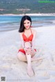 A woman in a red bikini sitting on the beach.