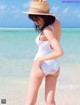 A woman in a white bathing suit and straw hat on the beach.