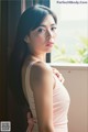 A woman in a pink dress leaning against a window.