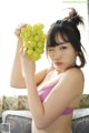 A woman in a pink bikini holding a bunch of grapes.