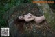 A naked woman laying on a rock in the woods.