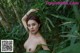 A naked woman standing in the middle of a lush green forest.