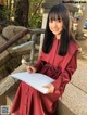 A woman in a red dress sitting on some steps holding a notebook.