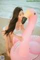 A woman in a white bikini standing next to a pink flamingo.