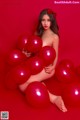 A woman sitting on a red surface surrounded by red balloons.