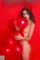 A naked woman holding red balloons in front of a red background.