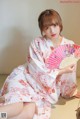 A woman in a kimono sitting on the floor holding a fan.