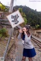 A woman in a school uniform standing next to a railroad track.