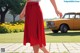 A woman in a red skirt walking down a sidewalk next to a car.