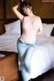 A woman in a pink bodysuit and jeans posing on a bed.