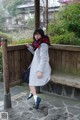 A woman leaning against a wooden fence wearing a gray coat.