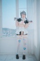 A woman in a maid outfit posing in front of a window.