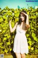 A woman in a white dress standing in front of a vineyard.