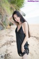 A woman in a black dress standing on a beach.